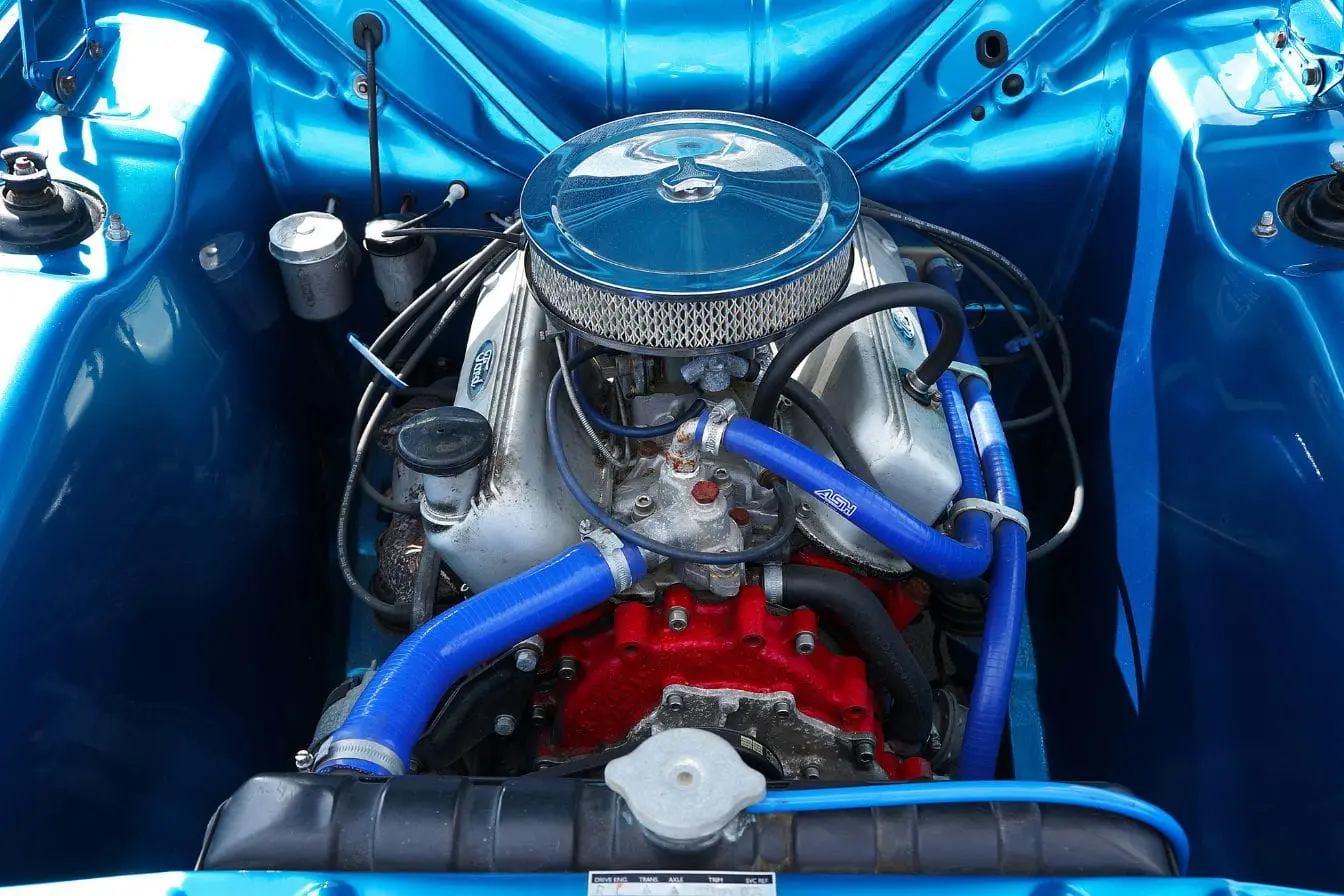 Vue détaillée d’un moteur Gros plan sur moteur avec durites bleues et pompe à eau, image évoquant les signes de défaillance à surveiller pour éviter une surchauffe.