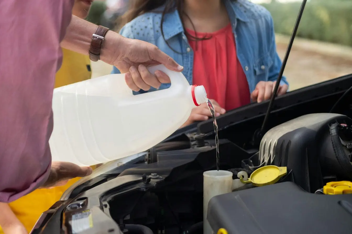 Vue moteur ouverte Gros plan sous capot, un conducteur verse du liquide dans le réservoir, illustrant la vérification et l’appoint du niveau de liquide de frein.
