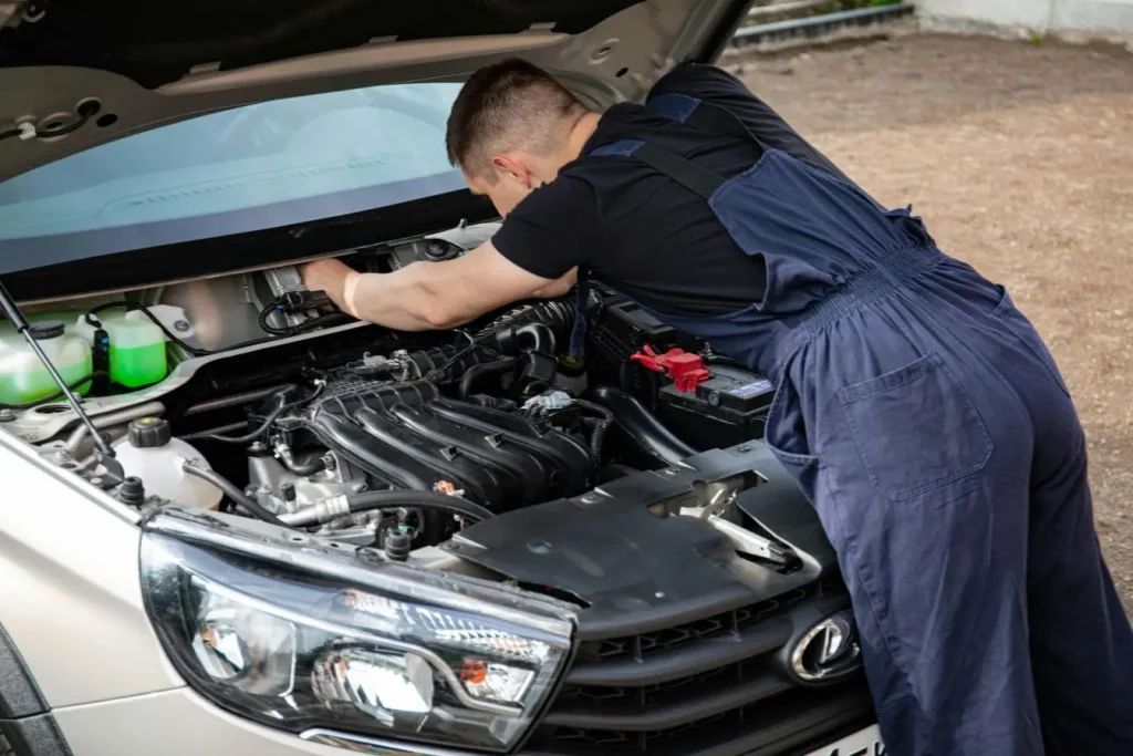 Mécanicien en bleu de travail penché sur moteur Lexus, image illustrant la recherche des signes de défaillance d’une pompe à eau.