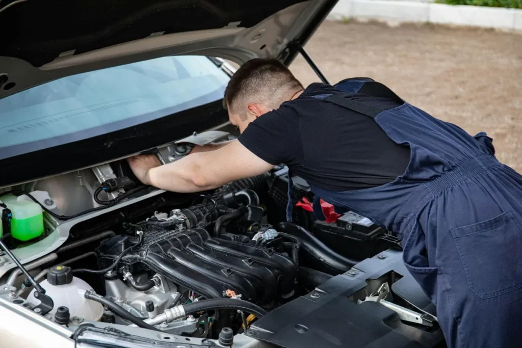 Mécanicien en bleu travaillant sous capot moteur, image illustrant le comparatif des frais d’entretien électrique et thermique.