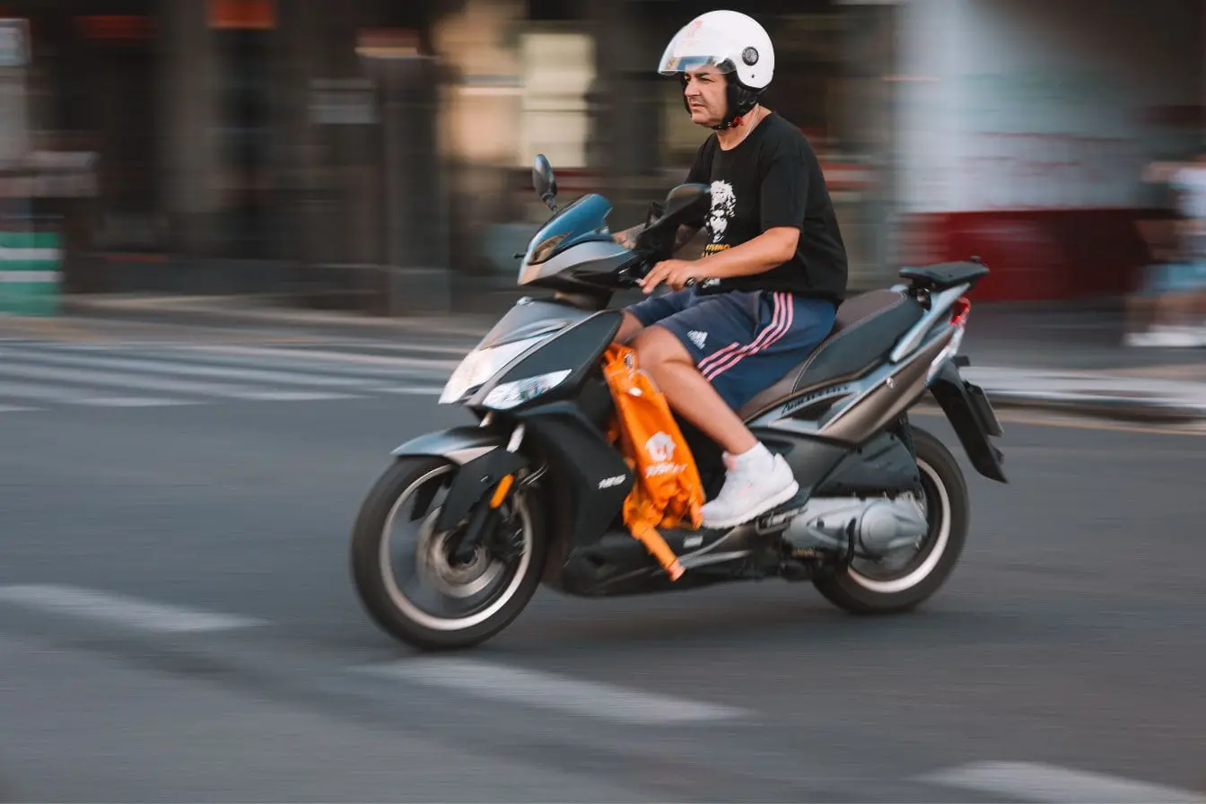 Scooter Personne en scooter noir portant casque blanc, image qui illustre la conduite urbaine liée au Permis AM Cyclomoteur.