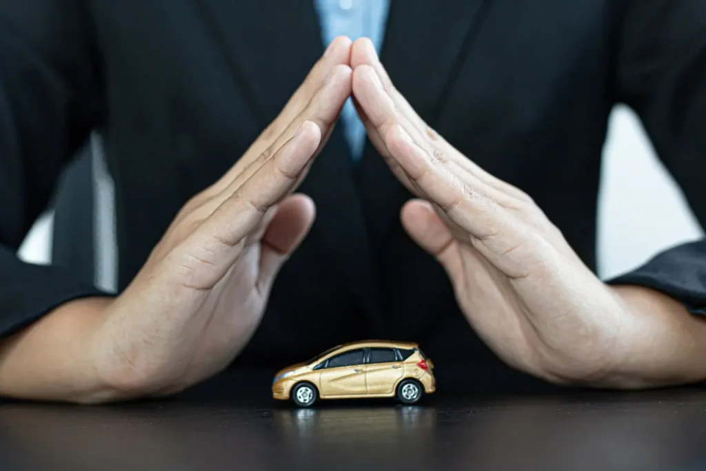 Mains en geste protecteur au-dessus d’une petite voiture dorée, image illustrant la notion d’indemnisation après dégâts causés par un nid de poule.
