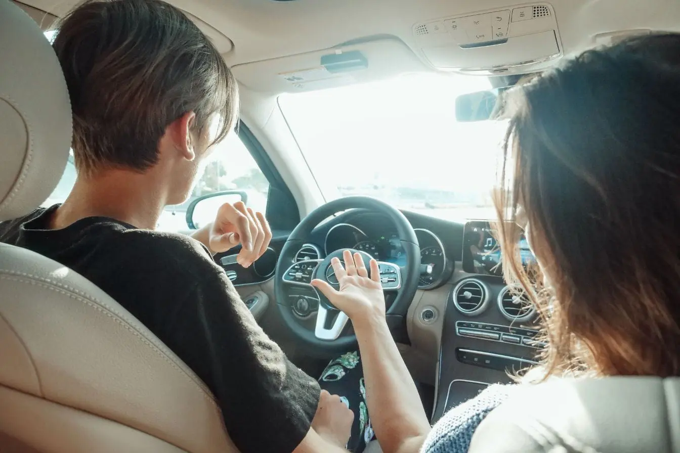 moniteur auto-école Deux personnes assises à l’avant d’une voiture discutent, image qui illustre l’apprentissage et le coût d’une formation de moniteur auto-école.