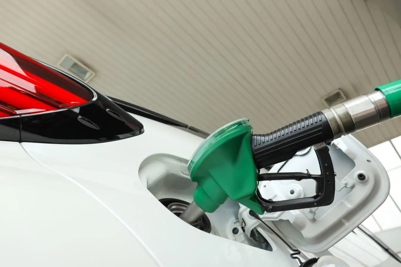 remplissage de réservoir Voiture blanche en station-service avec pistolet vert inséré, image illustrant l’usage d’additifs pour carburant moteur.