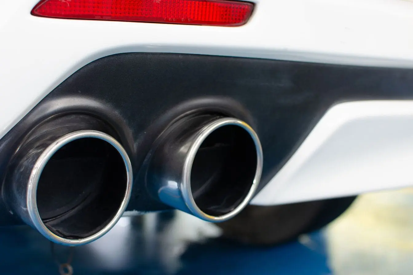 Pots d’échappement métalliques Vue arrière d’une voiture blanche avec double échappement poli, image qui illustre la réglementation encadrant la modification du pot d’échappement.
