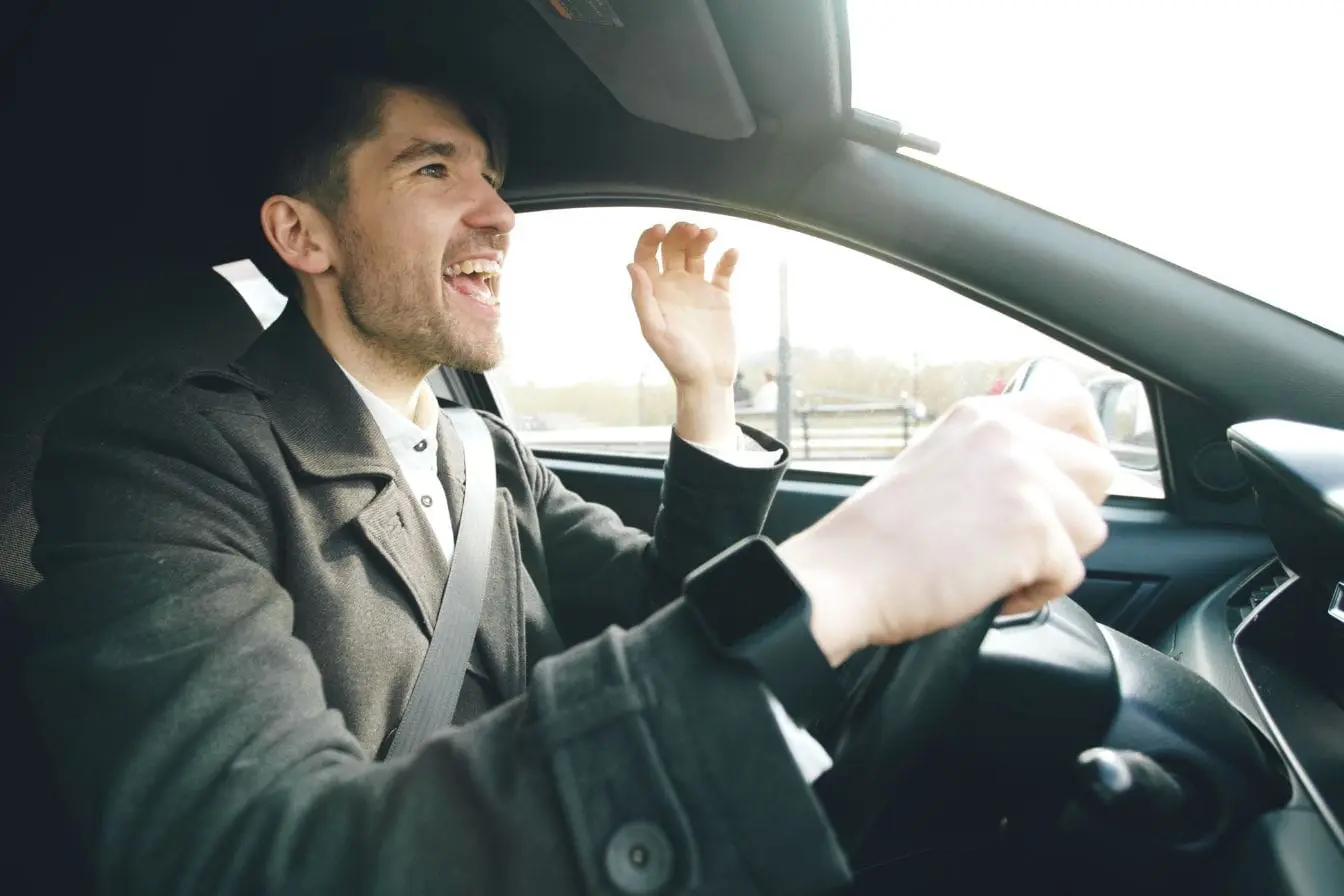 Gros plan sur conducteur en manteau sombre, image claire d’un geste pouvant évoquer le road rage.