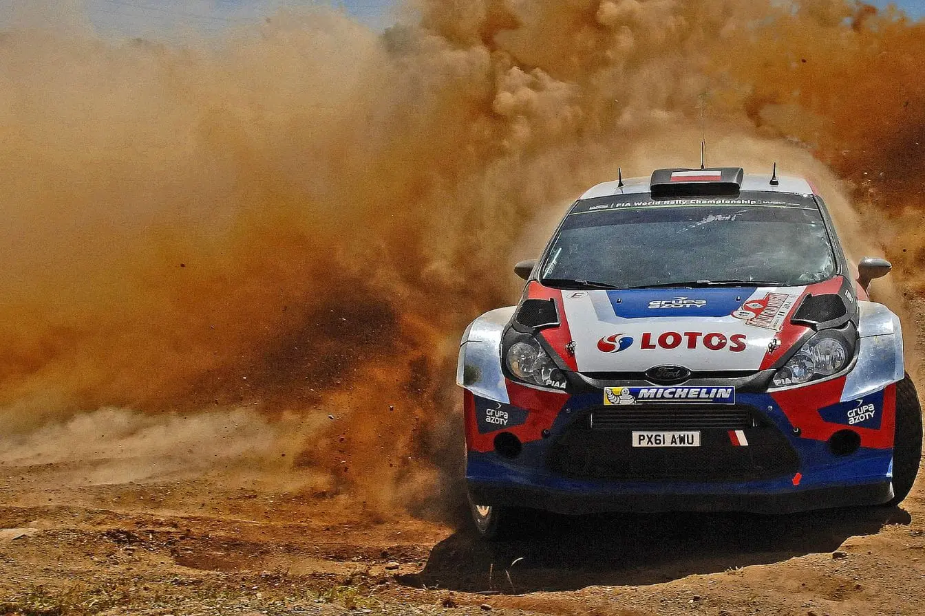 Voiture de rallye Voiture de rallye Ford décorée logos sponsors soulevant nuage de poussière, reflet de l’intensité du WRC face aux différences avec WRC2.