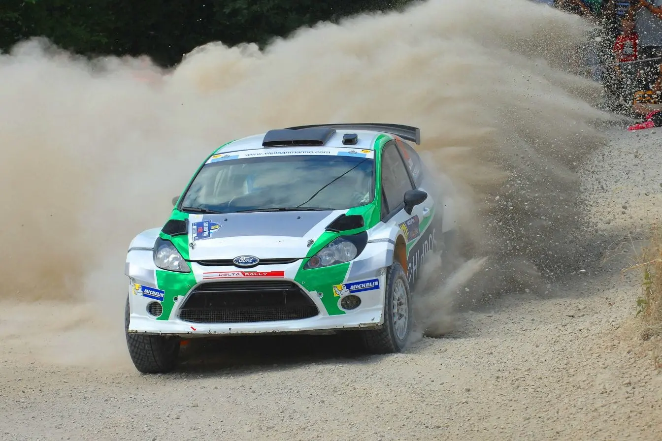 Voiture de rallye Ford filant sur piste de gravier, reflet de l’intensité et des défis pour devenir pilote de rallye.
