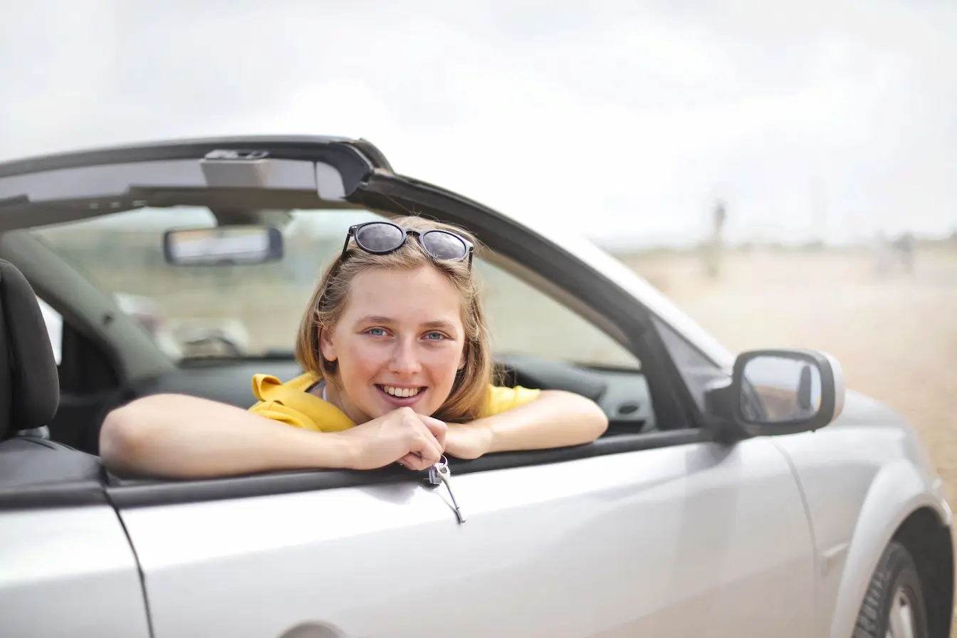 Personne en haut jaune tenant clé de voiture depuis cabriolet argenté, symbole de l’assurance auto temporaire pour usage ponctuel.